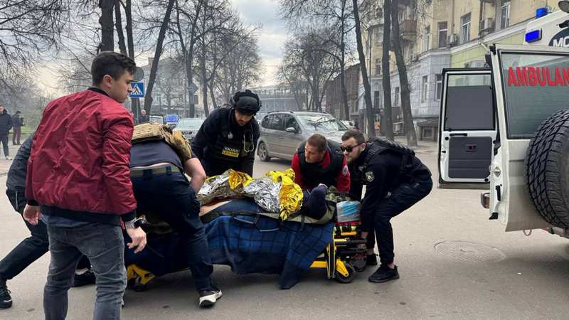 Рятувальники несуть пораненого на носилках до швидкої під час негоди в Україні