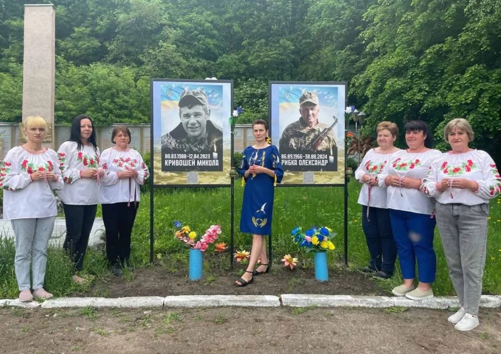 Жінки у вишиванках тримають стрічки пам’яті біля портретів полеглих героїв