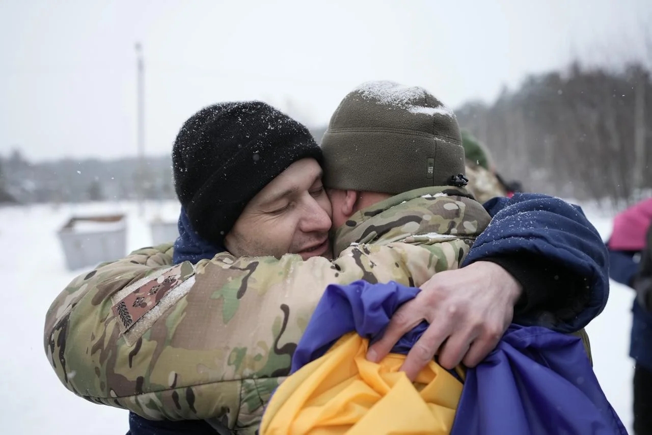 Звільнені українські полонені обіймаються з прапором після обміну з РФ