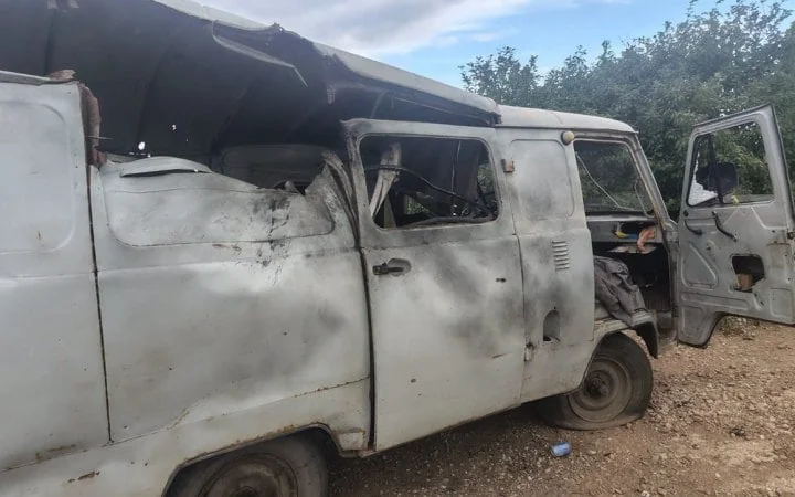 Обгорілий білий фургон з проваленим дахом і відчиненими дверима біля дерев
