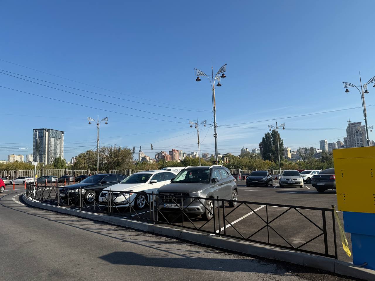 Автостоянка з сірими та білими авто на тлі київських багатоповерхівок