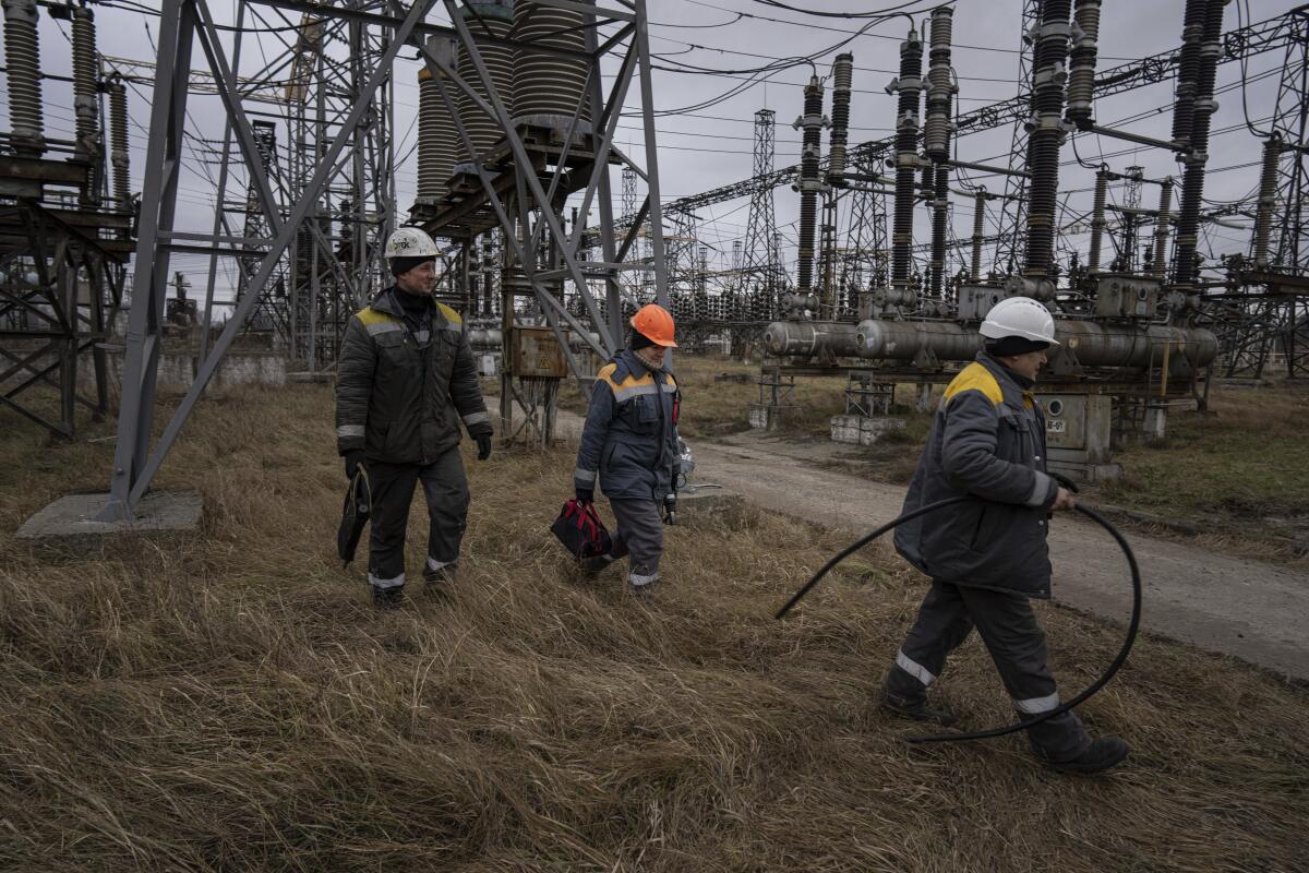 Троє енергетиків у касках йдуть полем біля високовольтних ліній електропередач