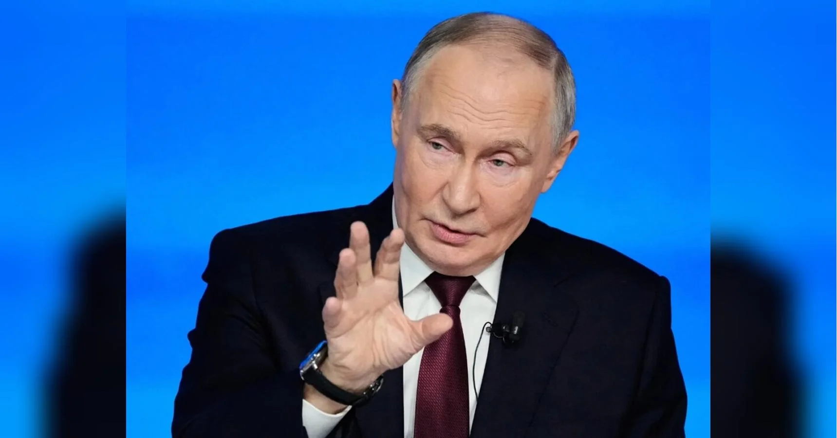 Володимир Путін жестикулює рукою під час виступу на синьому тлі